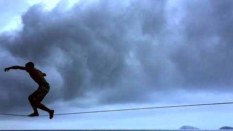 Silhouette of person on slackline in slow motion against cloudy skies in Rio de Janeiro Brazil Adlı Stok Video