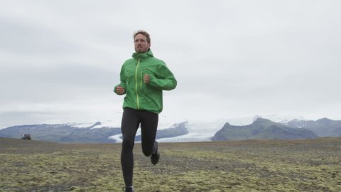 Male Runner. Tracking shot of male jogging and running on field. Determined athlete is in sports clothing. Majestic view of snowcapped mountains is in background. Fit fitness sports model. Stock Video