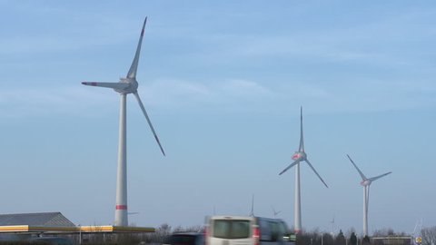 BERLIN, GERMANY - CIRCA 2014: Large windmill off German highway spinning and generating energy while cars below pass by on highway in Berlin, Germany.