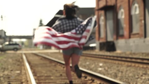 Teen Girl Runs Past Camera And Down Train Tracks, With American Flag (Slow Motion)