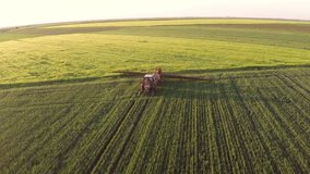 Tractor pulling a sprayer machine in wheat fields. Aerial footage.
