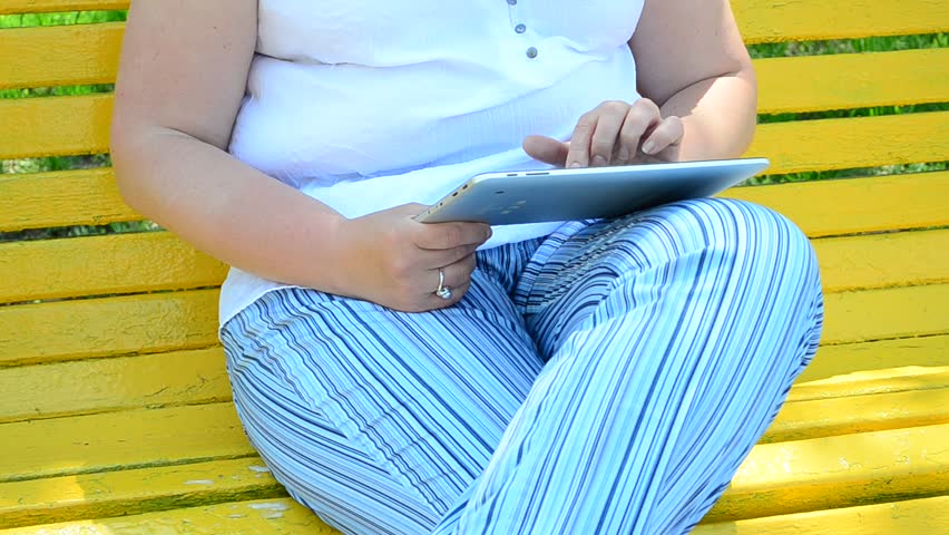 The girl sits on a bench in park with the tablet