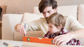 Lets do it together. Good-looking young dad sitting with his little son on couch and teaching him how to work with meter measure ruler
