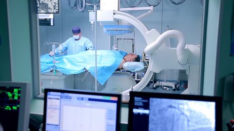 In an operation room a surgeon and a nurse make a surgery. The surgery is being controlled via monitors. 
