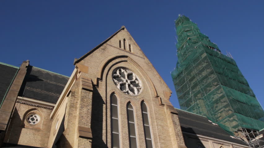 Large church undergoing renovations. Scaffolding surrounds the church tower and green wrap billows in the wind. Two shots. Toronto, Ontario, Canada.